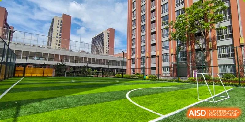 An outdoor view of a building at SHENGHUA ZIZHU ACADEMY overlooking a well-maintained green artificial turf field marked for sports.