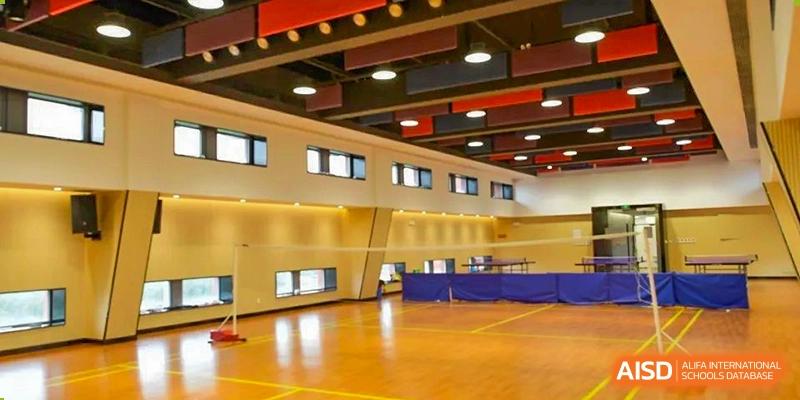 The interior of a large gymnasium or indoor sports hall at SHENGHUA ZIZHU ACADEMY with wooden flooring and bright lighting.