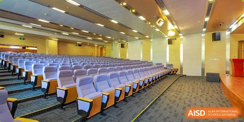 A large, modern auditorium or lecture hall at SHENGHUA ZIZHU ACADEMY with rows of purple tiered seating and warm lighting.