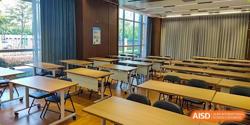 A bright, modern classroom at SHENGHUA ZIZHU ACADEMY with rows of individual desks and chairs next to large windows overlooking a green area.