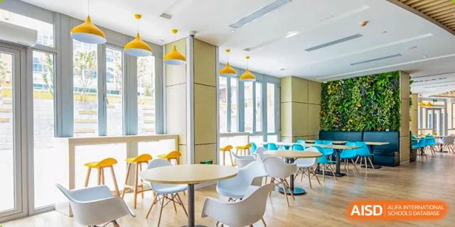 A bright, open student lounge or dining area at SHENGHUA ZIZHU ACADEMY with white round tables, modern chairs, and tall windows.