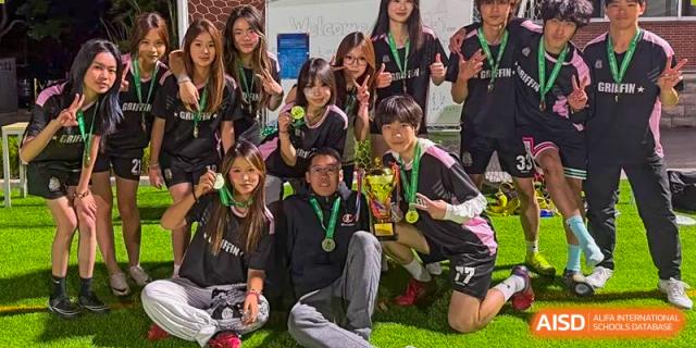 A group of students and an adult, possibly from a sports team or club at SHENGHUA ZIZHU ACADEMY, posing for a photo with medals and trophies on a grass field.
