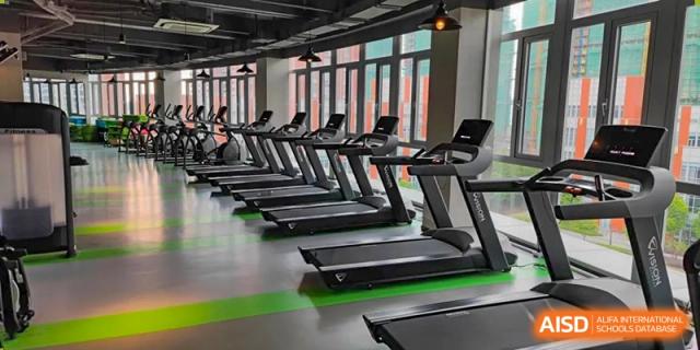 A modern fitness center or gymnasium at SHENGHUA ZIZHU ACADEMY with a row of treadmills facing large windows.