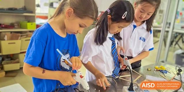 Students using a glue gun for a craft or building project at Shenzhen American International School.