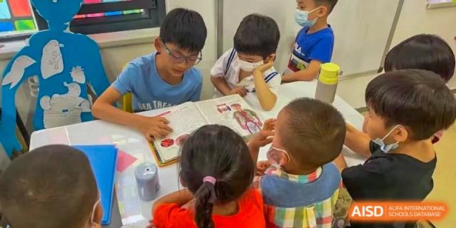 Young students collaborating and looking at a book or worksheet around a table at Shenzhen American International School.