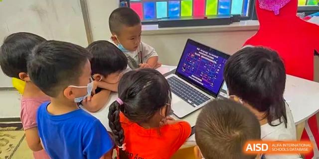 Young students gathered around a laptop, engaged in a technology or coding lesson at Shenzhen American International School.