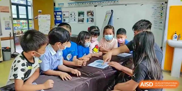 A group of young students, some wearing masks, working together on a tablet device at Shenzhen American International School.