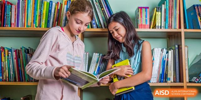 Two female students smiling while looking at a book on a bookshelf at Shenzhen American International School.