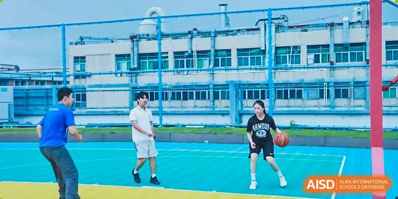 Two students playing a sport on an outdoor court with a school building in the background at Shenzhen American International School.