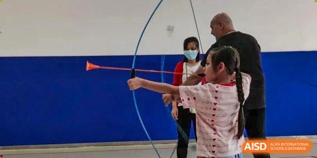A student practicing archery with a bow and arrow during an indoor sports activity at Shenzhen American International School.