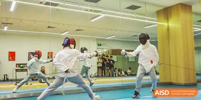 Students wearing protective gear and fencing in an indoor sports area at Shenzhen American International School.