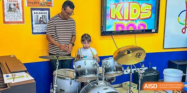 A young student playing a drum set in a music class or studio at Shenzhen American International School.