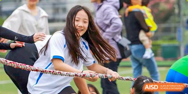 A female student smiling while participating in a tug-of-war game during a school field day at Shenzhen American International School.