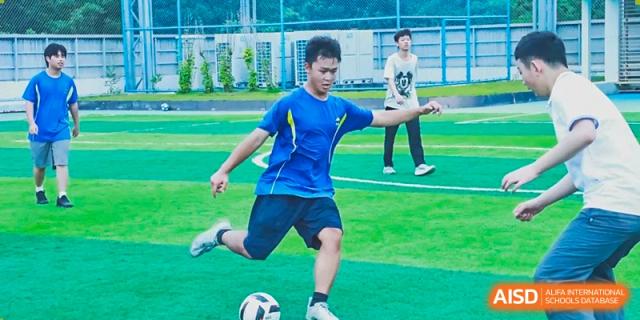 A student in a blue uniform kicking a soccer ball on an outdoor turf field at Shenzhen American International School.