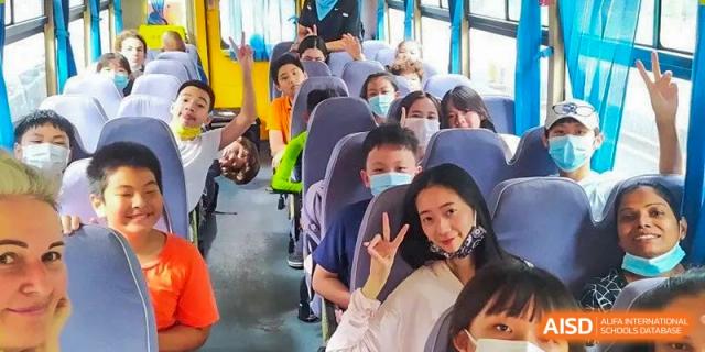 A student smiling and giving a peace sign while riding a school bus with other students wearing face masks at Shenzhen American International School.