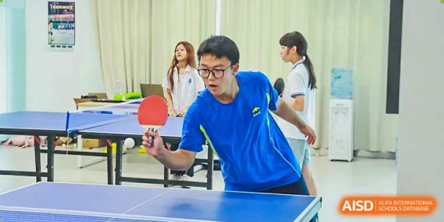 A male student holding a paddle and preparing to hit a ball during a game of table tennis at Shenzhen American International School.