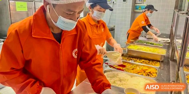 Canteen staff serving food to students from a buffet line at Shenzhen American International School.