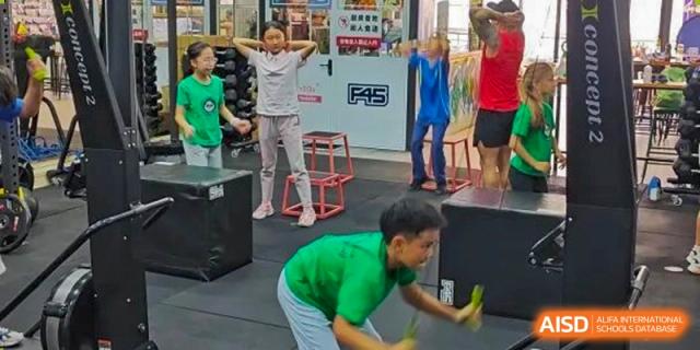A student in a green shirt doing a floor exercise while a teacher supervises nearby in the gym at Shenzhen American International School.