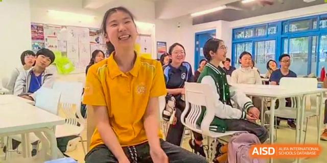 A female student in a yellow shirt smiling brightly while sitting with classmates in a classroom at Shenzhen College of International Education.