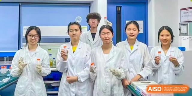 Three students in white lab coats posing with equipment in a science laboratory at Shenzhen College of International Education.