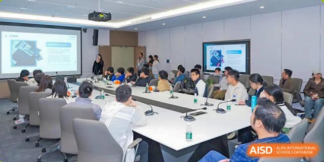 Students and teachers seated around a large white conference table in a modern meeting or lecture room at Shenzhen College of International Education.