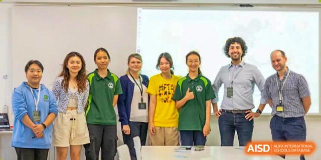 A group of diverse students and an adult posing together in a classroom or school setting at Shenzhen College of International Education.