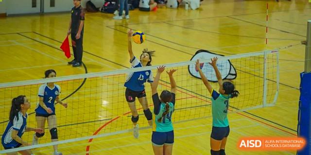 A female student jumping to spike a volleyball over the net during a game at Shenzhen College of International Education.