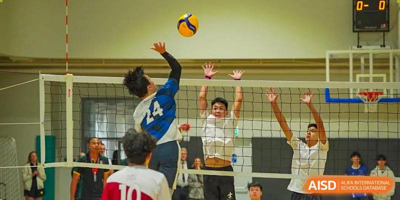 A male student jumping to hit a volleyball over the net during an intense match at Shenzhen College of International Education.