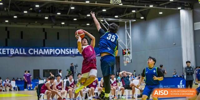Two male students jumping high to contest a shot during a basketball game at Shenzhen College of International Education.