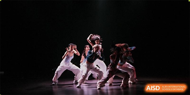 A group of students performing a modern or contemporary dance routine on a dark stage at Shenzhen College of International Education.