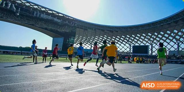 Students playing an active outdoor game, possibly soccer or tag, on a paved court at Shenzhen College of International Education.