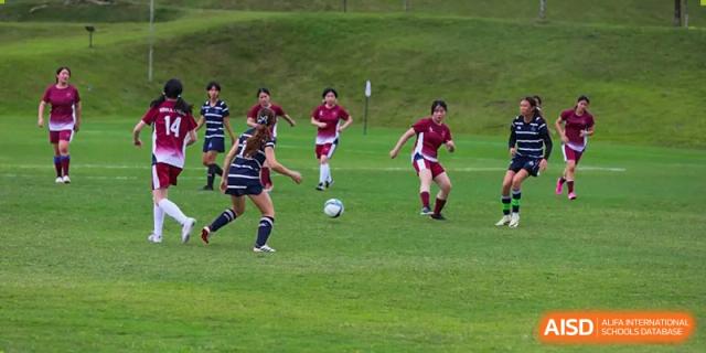 Female students playing an outdoor soccer match on a grass field at Shenzhen College of International Education.