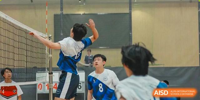 A student reaching up to hit a ball during an indoor volleyball or basketball game at Shenzhen College of International Education.