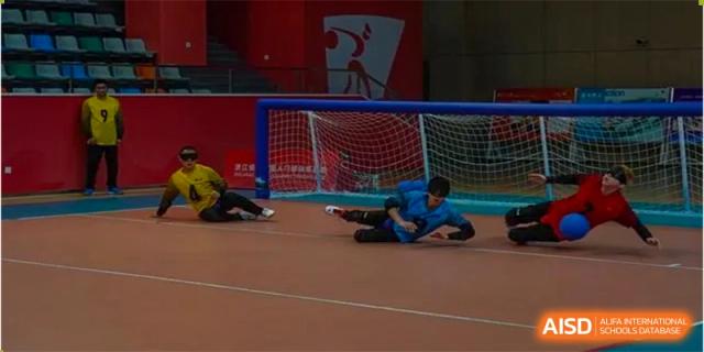A goalkeeper in blue diving to save a goal on an indoor soccer pitch at Shenzhen College of International Education.