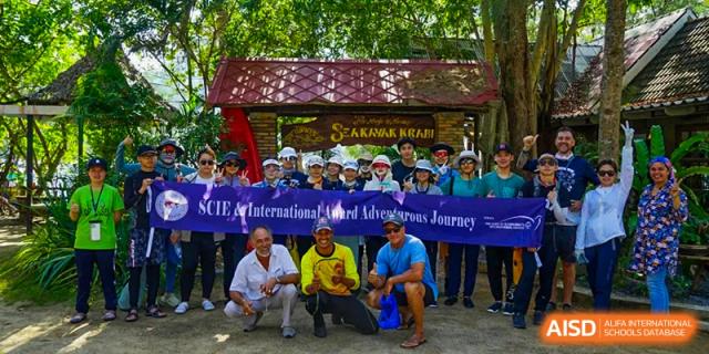 A group of students and adults posing outdoors with a banner, possibly after an adventure or international trip, at Shenzhen College of International Education.
