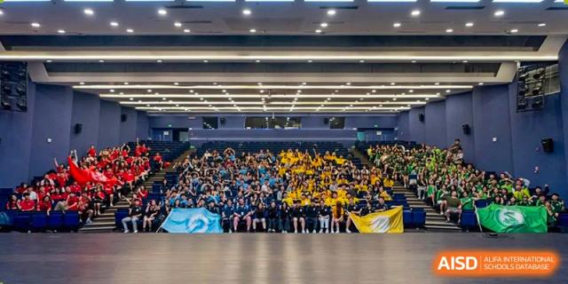 A crowd of students and athletes gathered in a large, well-lit indoor gymnasium for a sports event at Shenzhen College of International Education.