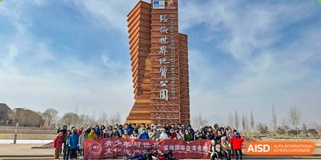 A large wooden tower structure with people and a banner in the foreground at Shenzhen College of International Education.
