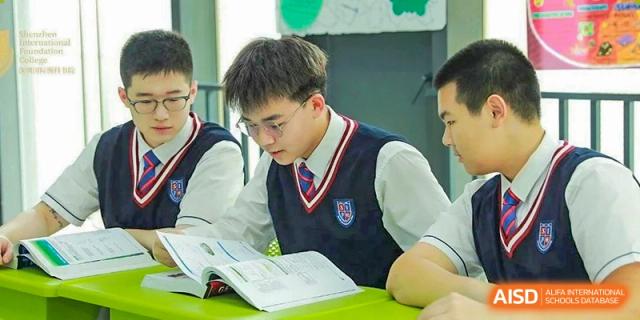 A male student in school uniform reading a textbook while sitting at his desk at Shenzhen International Foundation College (SIFC).