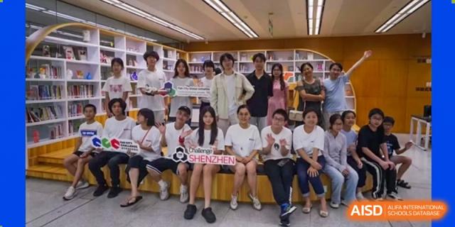 A group of students in white shirts posing with a banner that reads "COLLEGE OF SHENZHEN" at an event at Shenzhen International Foundation College (SIFC).