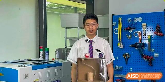 A male student in uniform presenting a science or engineering project with physical models in the classroom at Shenzhen International Foundation College (SIFC).