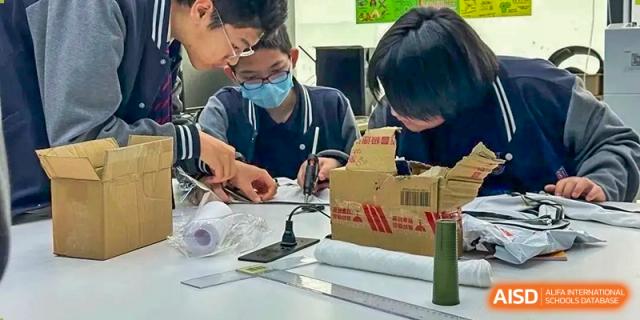 Students collaborating on a hands-on project, possibly involving wiring and design, at Shenzhen International Foundation College (SIFC).