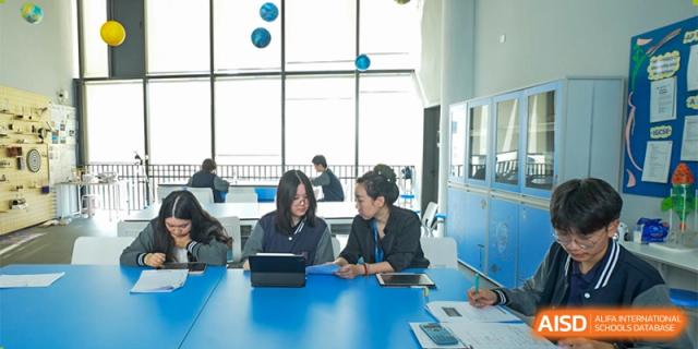 Students collaborating in a study group using tablets and laptops at a bright blue table at Shenzhen International Foundation College (SIFC).