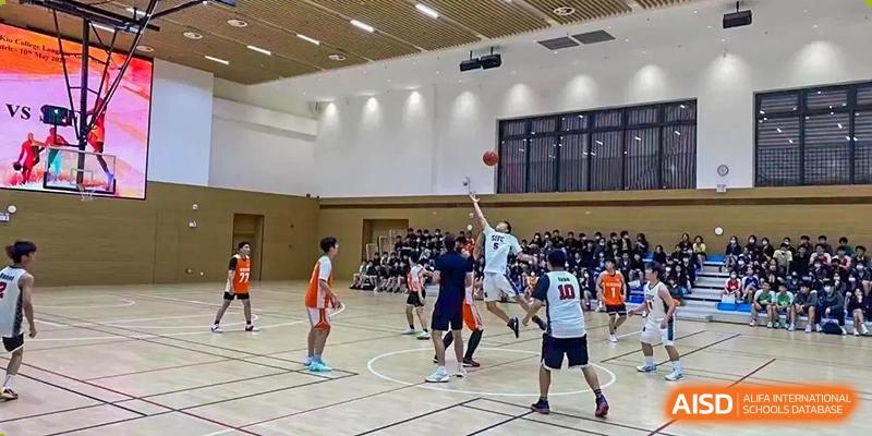 Students playing a basketball game in a large, well-lit indoor gymnasium at Shenzhen International Foundation College (SIFC).
