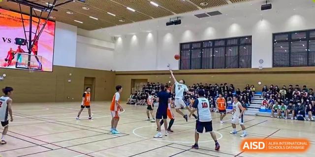Students playing a basketball game in a large, well-lit indoor gymnasium at Shenzhen International Foundation College (SIFC).