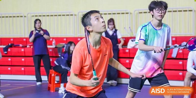 A student in an orange shirt concentrating while playing badminton in an indoor court at Shenzhen International Foundation College (SIFC).