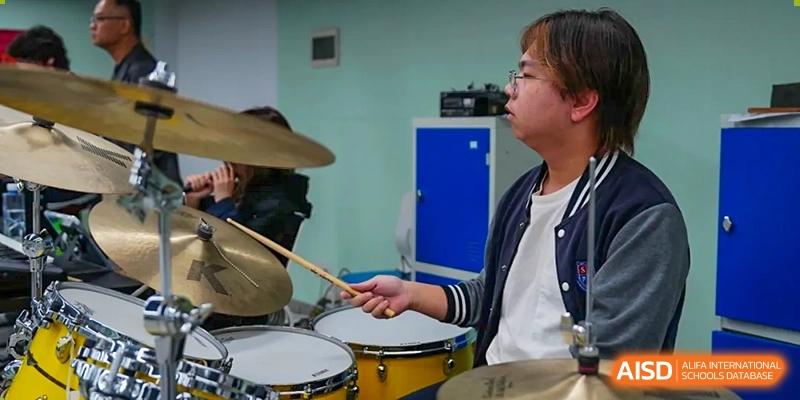 A student playing the drums as part of a band or music practice at Shenzhen International Foundation College (SIFC).