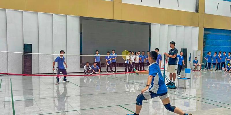 A student preparing to serve or receive the ball during an indoor volleyball or badminton game at Shenzhen International Foundation College (SIFC).