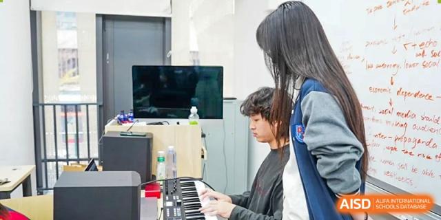 Two students collaborating on a music project, with one playing a keyboard and the other looking at a screen at Shenzhen International Foundation College (SIFC).