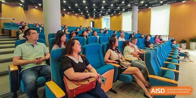 An audience of students and adults sitting in blue auditorium seats attending a lecture or presentation at Shenzhen International Foundation College (SIFC).