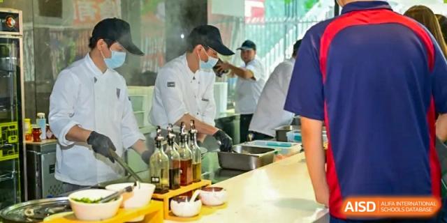 Chefs and kitchen staff preparing food with various bottles of oil and seasoning on a counter at Shenzhen International Foundation College (SIFC).